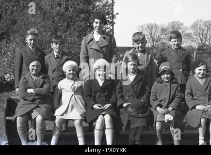 1940, historique, photo de classe de l'école primaire, groupe d'écoliers britanniques dans leur meilleur vestes, manteaux et chapeaux, line-up ensemble en dehors de la classe pour une photographie avec leur professeur, England, UK. Banque D'Images