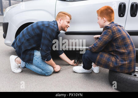Père avec un cric de voiture de levage pour changement de pneu, fils de le regarder Banque D'Images