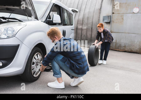 Père changer pneu en voiture avec clé de roue, son holding tire Banque D'Images