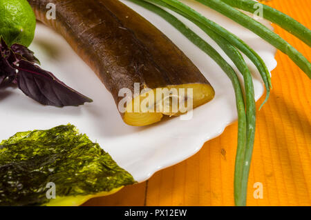 Still Life - orphie fumé avec de la chaux, le basilic, l'oignon vert, chili, nori chips, épices, huile d'olive dans un plat de céramique blanc, sur une table en bois Banque D'Images