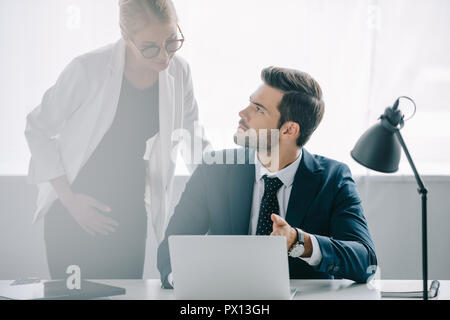 Portrait de femme enceinte et collègue de travail avec ordinateur portable à discuter en fonction du projet Banque D'Images