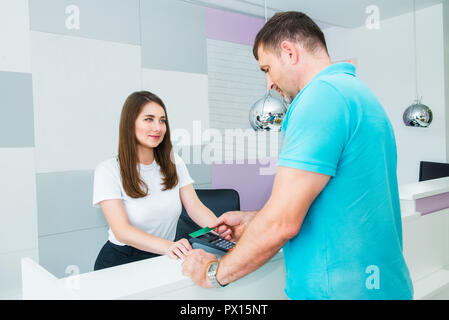 Client déposant le paiement sans contact avec la technologie NFC carte de crédit au magasin, clinique, hôtel. Gestionnaire administratif avec terminal de point de vente à l'accueil de Banque D'Images