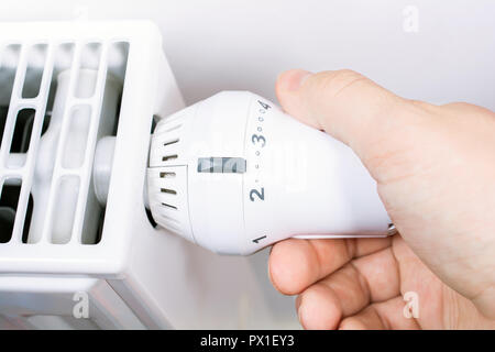 La main d'un homme tourne le radiateur de chauffage d'un livre blanc dans le salon, concept d'économiser de l'énergie Banque D'Images