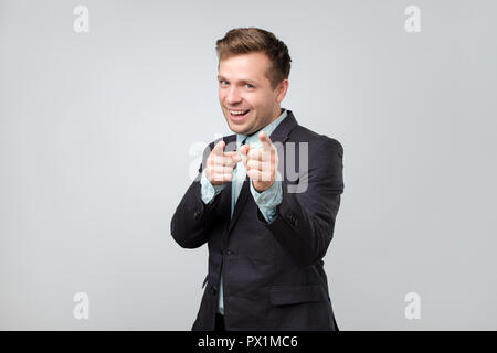 Studio portrait of handsome young guy en fonction de l'expression des émotions positives tout en montrant des signes d'armes à feu avec l'index comme si dire bonjour ou comment vous d Banque D'Images