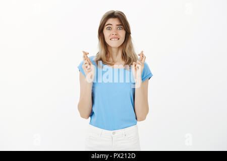 Portrait de femme attrayante intense inquiets en tee-shirt bleu, soulevant les doigts croisés et de mordre la lèvre, les sourcils, se sentir nerveux et incertain tout en rendant le souhaitent ou l'espoir d'obtenir la promotion au travail Banque D'Images