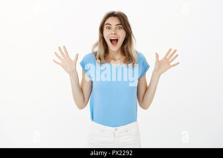 Portrait de heureux heureux jolie femme avec les cheveux clairs, criant et agitant soulevé de palmiers des émotions positives, la réception et l'incroyable surprise fantastique, debout sur fond gris Banque D'Images