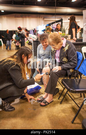 Les femmes âgées à pieds endoloris essayer avec une batterie de secours électronique powered stick-on stimuler l'appareil à une amélioration de l'exposition à Costa Mesa, CA. Banque D'Images