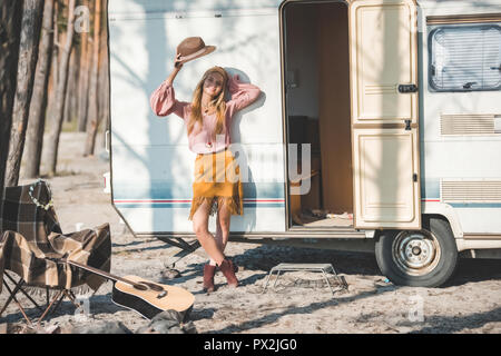 Jeune femme hippie avec hat posing près de remorque avec guitare en forêt Banque D'Images