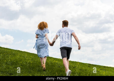 Vue arrière du rouquin couple holding hands and running on grassy hill Banque D'Images