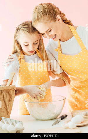 Smiling mother et adorable petite fille en jaune à pétrir la pâte des tabliers sur Rose Banque D'Images