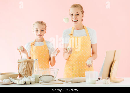Heureuse mère et fille jonglant avec des morceaux de la pâte pendant la cuisson isolé sur pink Banque D'Images
