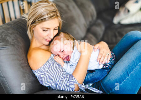 Jeune maman avec bébé fille sur le canapé à la maison, le bébé qui pleure Banque D'Images