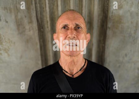 Senior homme chauve touristiques contre vieux mur de béton Banque D'Images