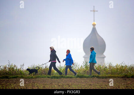 19 octobre 2018, Bade-Wurtemberg, Unlingen-Göffingen : trois marcheurs passer un tour de l'église dans le brouillard peu après le lever du soleil. Photo : Thomas/Warnack dpa Banque D'Images