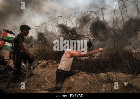 Palestiniens manifestant vu holding la clôture alors que le noir de la fumée des pneus en feu en soufflant de l'air au cours des affrontements. Des affrontements entre Palestiniens et Israël à la frontière de Gaza. Banque D'Images