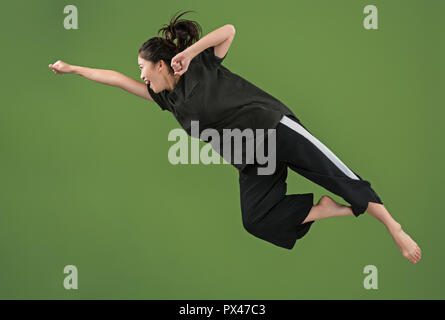 Je suis heureux. L'air shot of pretty smiling young woman jumping et gesticulant contre green studio arrière-plan. Shining girl en mouvement ou mouvement. Les émotions humaines et les expressions faciales concept Banque D'Images