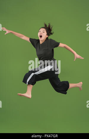 Je suis heureux. L'air shot of pretty smiling young woman jumping et gesticulant contre green studio arrière-plan. Shining girl en mouvement ou mouvement. Les émotions humaines et les expressions faciales concept Banque D'Images