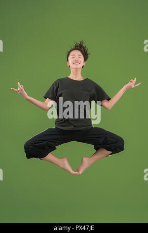 Je suis heureux. L'air shot of pretty smiling young woman jumping et gesticulant contre green studio arrière-plan. Shining girl en mouvement ou mouvement. Les émotions humaines et les expressions faciales concept Banque D'Images