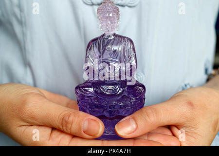 Femme bouddhiste avec une figurine en plastique violet d'un Bouddha assis dans les mains. Notre annuaire d'entreprises. Le Vietnam. Banque D'Images