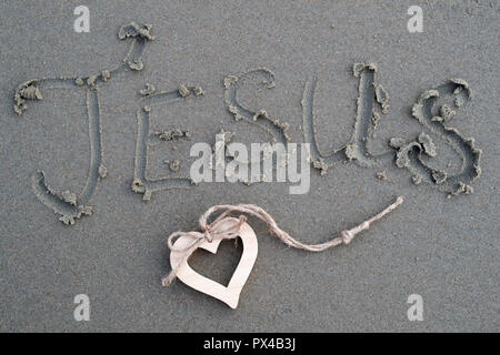Un coeur en bois et le nom de Jésus écrit dans le sable. Banque D'Images