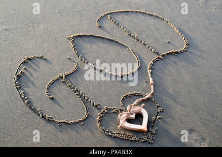 Un coeur en bois et le nom de Dieu écrit dans le sable. Banque D'Images