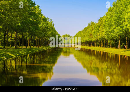 Un canal d'eau bordé de deux avenues d'arbres dans le parc Karlsaue à Kassel, Allemagne. Belle scène de visiteurs de marcher sous les arbres, reflétée sur... Banque D'Images