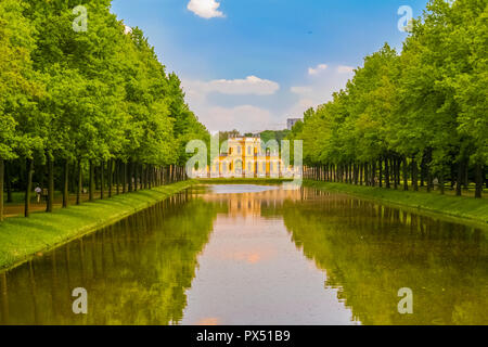 Vue pittoresque sur un canal d'eau avec des voies gauche et droite et une orangerie style baroque, dans le centre. Les arbres et le ciel bleu sont... Banque D'Images