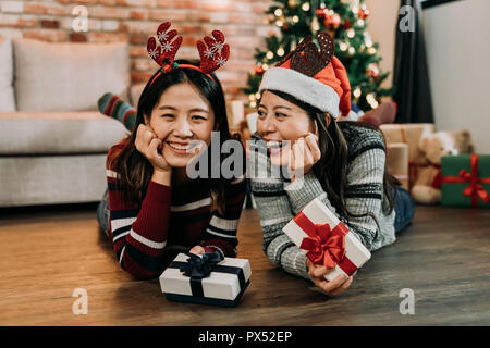 Deux amis portant sur le plancher en bois de célébrer Noël à la maison de Noël. fille avec chaussettes colorées et de chapeaux de l'échange de cadeaux. jolies filles holdi Banque D'Images