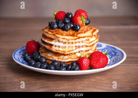 Pile de crêpes aux bleuets frais, fraises et sirop d'érable sur une plaque bleu et blanc Banque D'Images