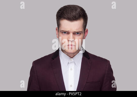 Closeup portrait of angry beau jeune homme en costume violet et chemise blanche, debout et à la caméra à l'agressif avec mauvaise humeur. Piscine studio sh Banque D'Images