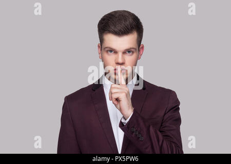 Portrait de grave beau jeune homme en costume violet et chemise blanche, debout, looking at camera with silence signe et avertissement. piscine, studio shot Banque D'Images