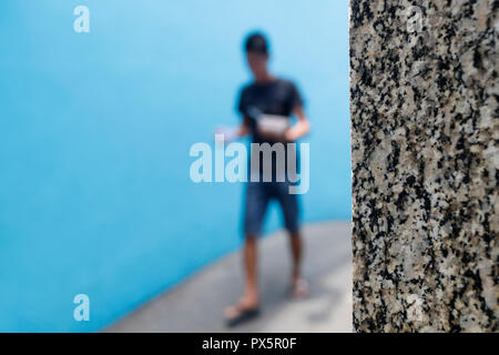 Garçon marchant sur une petite rue contre un mur bleu. Homme marchant sur une petite rue contre un mur bleu. Ho Chi Minh Ville. Le Vietnam. Banque D'Images