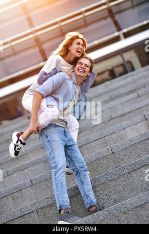 Homme donnant à sa jolie petite amie une piggy back at street Extreme sur une journée ensoleillée. Banque D'Images