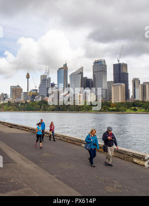 Les piétons marchant sur le long chemin Farm Cove Le Port de Sydney avec les immeubles de bureaux et de la CDB sur l'horizon un jour nuageux Sydney NSW Australie. Banque D'Images