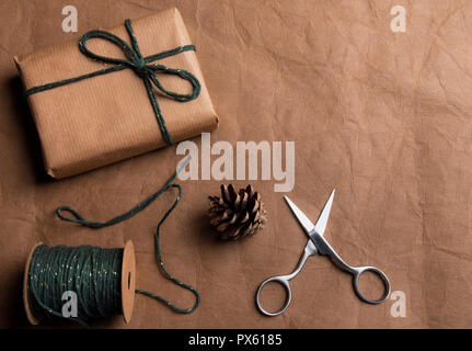 Cadeaux concept avec un cadeau enveloppé dans du papier classique brun, une boule de ficelle verte et ciseaux sur un fond de cuir brun. Banque D'Images