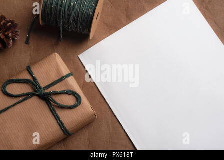 Boîte-cadeau enveloppé dans du papier brun classique, à égalité avec le vert et l'or string et un accord tacite livre blanc sur une base de cuir. Banque D'Images