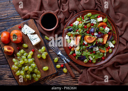 Salade d'automne délicieux avec du chocolat, kaki, moule fromage bleu raisin vert, tranches de prune et la roquette sur une plaque de faïence avec des ingrédients sur une Banque D'Images