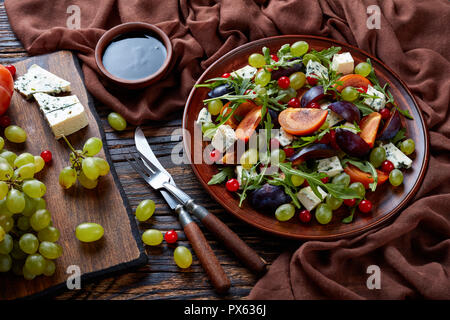 Salade d'automne délicieux avec du chocolat kaki, fromage bleu, raisin vert, tranches de prune et la roquette sur une plaque de faïence avec des ingrédients sur un cutti Banque D'Images