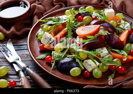 Close-up of delicious salade d'automne au chocolat avec moule bleu kaki, fromage, raisin vert, tranches de prune et la roquette sur une plaque de faïence avec ingrédients Banque D'Images