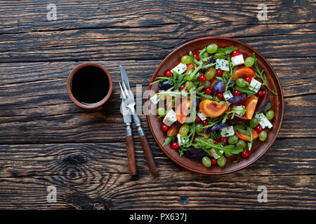Vue supérieure de l'automne délicieux chocolat salade de kaki, moisissure bleue fromage, raisins verts, de prune et de tranches de roquette sur une plaque de faïence sur un Banque D'Images