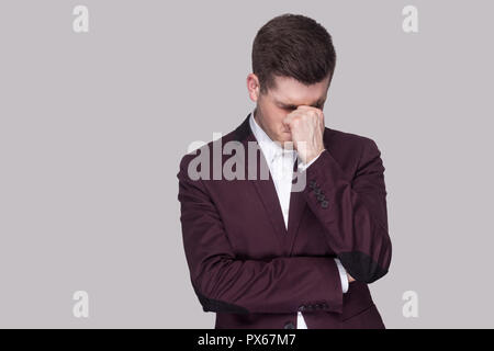 Portrait de triste déprimé beau jeune homme en costume violet et chemise blanche, debout tenant la tête en bas et les mains sur le visage et pleurer. Piscine studio sh Banque D'Images