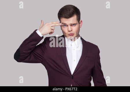 Portrait de confondre beau jeune homme en costume violet et chemise blanche, debout, looking at camera avec sérieux et geste des armes à feu. Piscine studio s Banque D'Images
