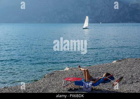 Cassone, Lac de Garde, Italie. Woman relaxing et bronzer dans un fauteuil confortable, sur la plage du lac de Garde près de Cassone Banque D'Images