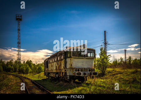 Vieux cimetière de locomotives diesel en train à l'été avec l'herbe verte et des arbres en arrière-plan et grand ciel nuageux Banque D'Images