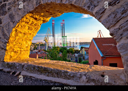 Ville de Pula et la côte de grues de chantier naval vue du coucher de soleil à travers la fenêtre en pierre, région de Croatie Istrie Banque D'Images