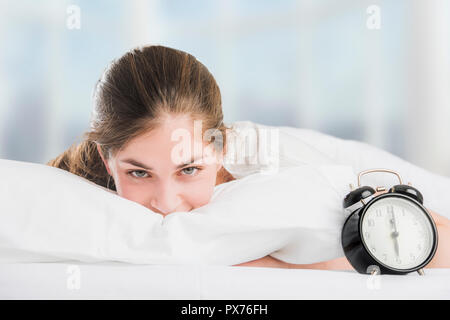 Une belle jeune femme au lit, se réveillant le matin heureusement à côté d'un réveil Banque D'Images