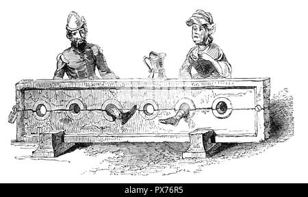 Un homme et une femme qui a eu lieu à l'époque médiévale, les stocks de dispositifs de retenue qui étaient utilisés comme une forme de châtiments corporels et l'humiliation publique. Elles consistaient à de grandes planches de bois avec charnières pour retenir les pieds. Les victimes peuvent être insulté, frappé, tickled, crachats, ou victimes d'autres actes inhumains. Banque D'Images