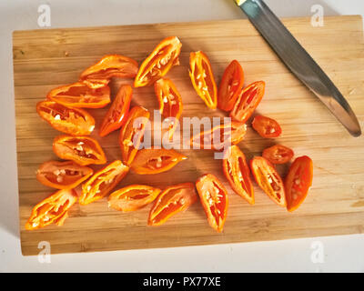 Shot de Naga Morich orange poivrons sur une planche à découper, en tranches avec un couteau Banque D'Images