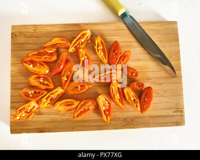 Shot de Naga Morich orange poivrons sur une planche à découper, en tranches avec un couteau Banque D'Images