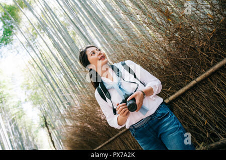 Tenir l'appareil photo photographe élégant debout à côté de la forêt de bambou. transport nature lens men girl enjoying view dans les montagnes. de Green Park à Kyoto Banque D'Images